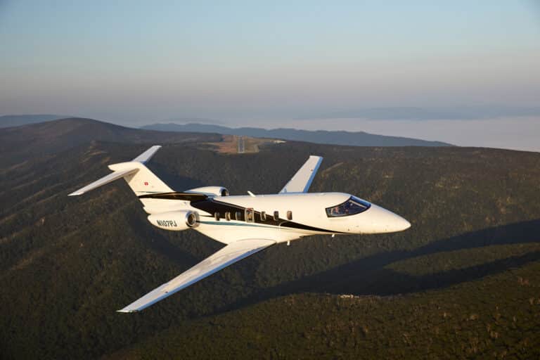 a pilatus pc-24 in flight with mountains in the background